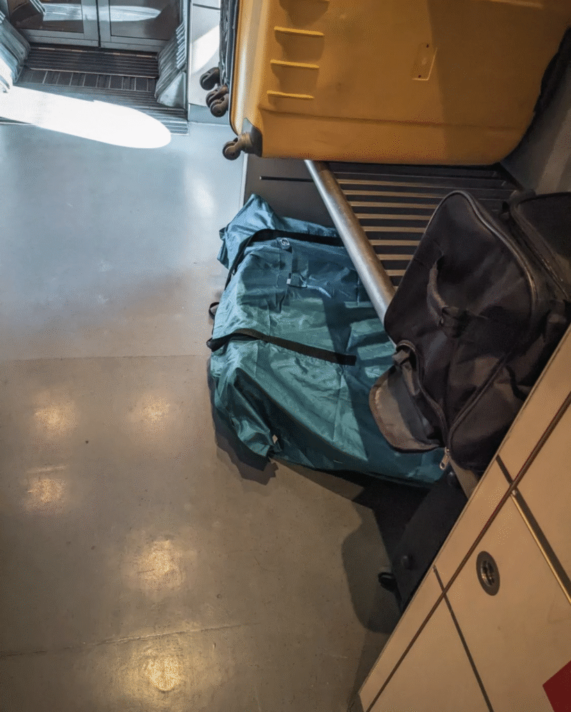 Bike bag with a bicycle stored beneath a luggage shelf on a train, surrounded by suitcases.