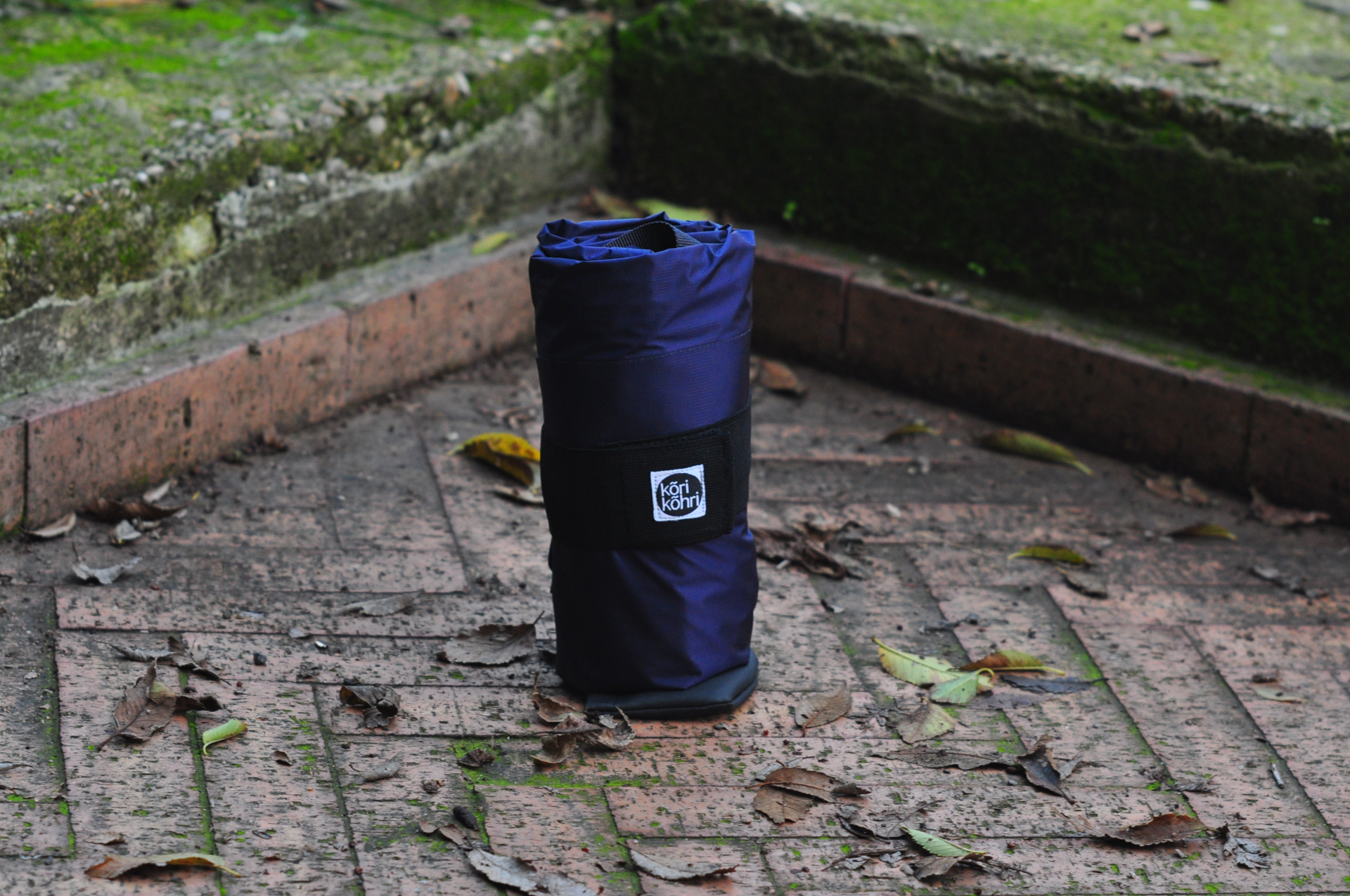 Rolled‑up Korikohri folding bike travel bag secured with logo strap
